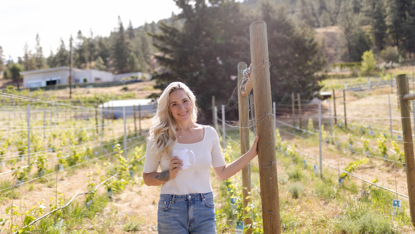 Woman standing in vineyard with trees and a farm in the background