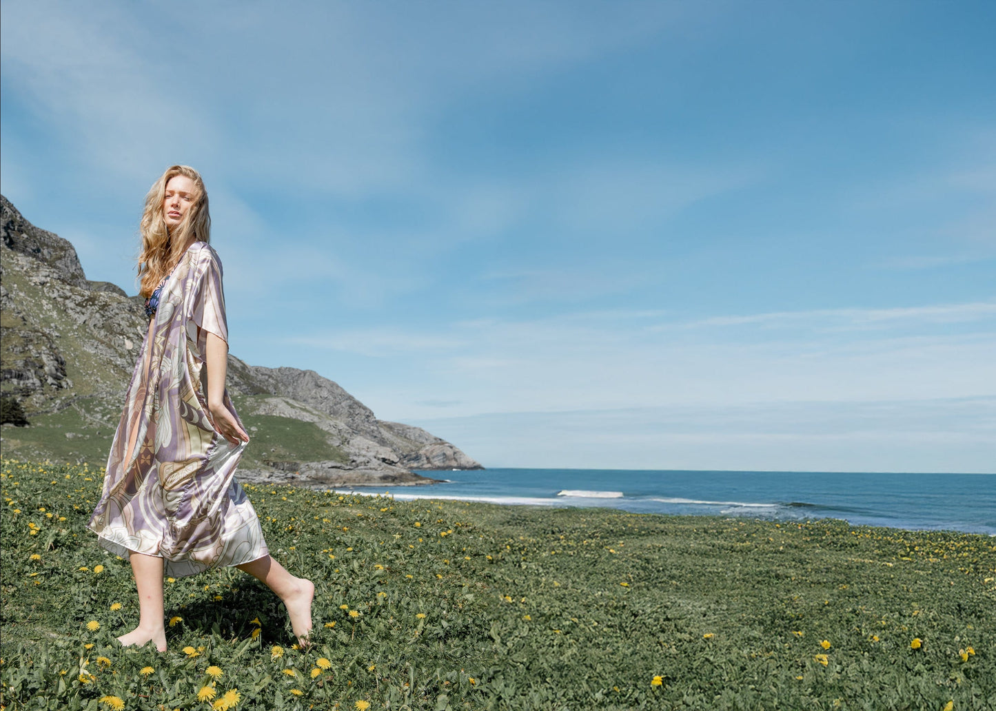 Woman in an art of marina nu boheme kimono standing on a grassy hill with ocean and mountains in the background